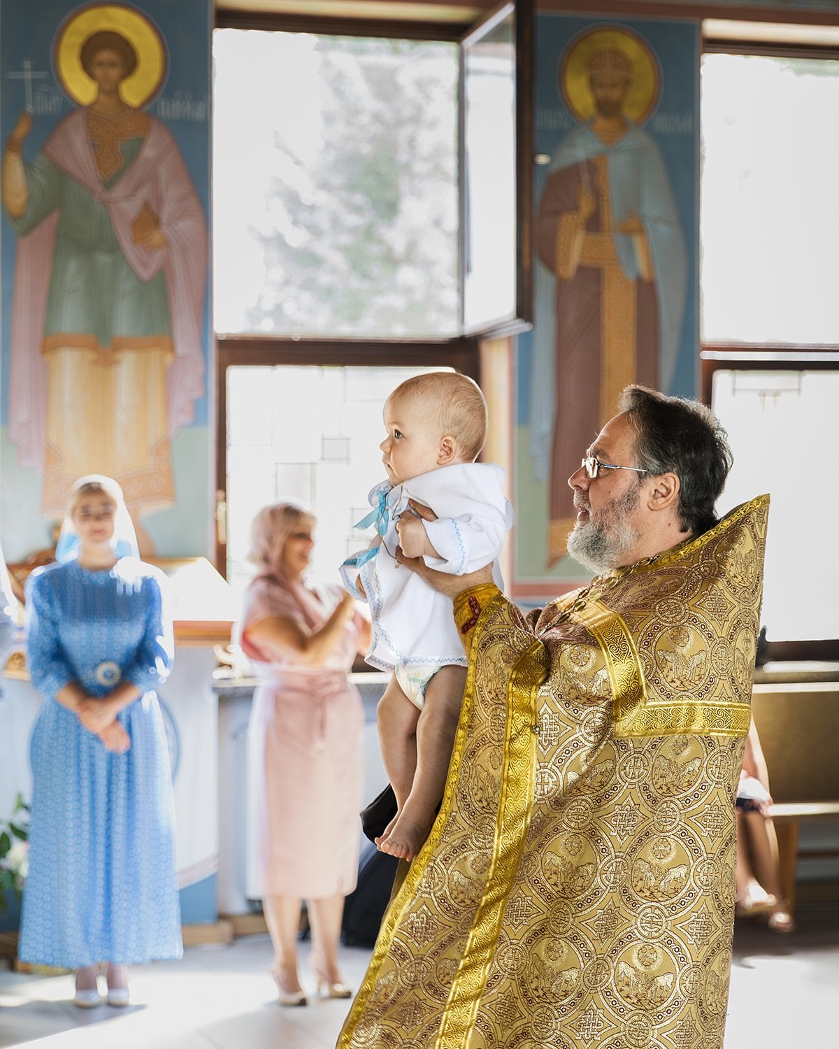 Priester hält das Taufkind vor den Ikonen der Kirche